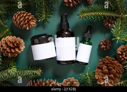 Pots en verre brun près des branches de sapin et des cônes de pin sur la vue de dessus vert foncé. Maquette d'emballage de marque. Produit de beauté pour les soins de la peau, crème ou sérum. Soins de santé Banque D'Images