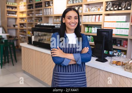 Portrait de jeune femme souriante Barista caucasien avec les bras croisés debout au café-restaurant. Unaltered, culture de café, les gens et l'occupation concept. Banque D'Images