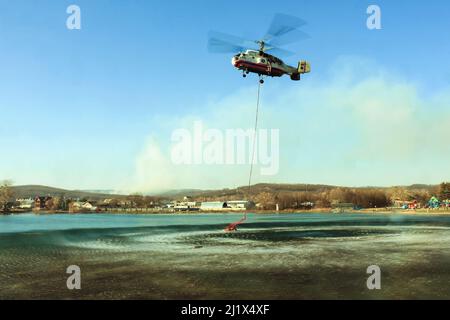 Un hélicoptère KA-32 du ministère des situations d'urgence survolant un lac d'où l'eau est aspirée pour éteindre un feu de forêt. Dans le backgrou Banque D'Images