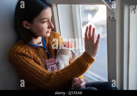 Une jeune fille ukrainienne triste et réfugiée a perdu sa maison et regarde par la fenêtre. Concept de guerre d'Ukraine. Banque D'Images