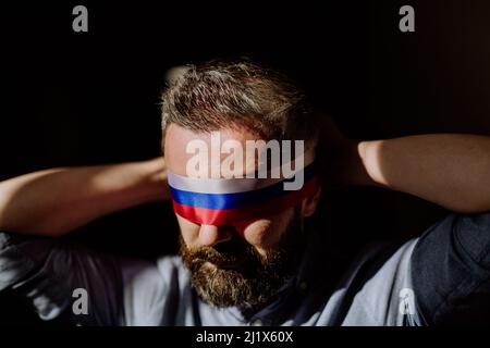 Homme avec le drapeau russe aveuglement sur fond noir, la propagande russe fermé les yeux des gens concept. Banque D'Images