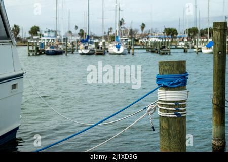 La corde marine en nylon, bleue et blanche, est attachée à un yacht et est soigneusement enroulée autour d'un poteau en bois sur une jetée de marina. Banque D'Images