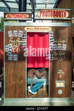 Vêtu de façon décontractée, adulte de race blanche non identifiable, s'accroupidant dans une cabine photo. Banque D'Images