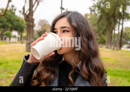 Buvez du café, une jeune femme très belle qui boit du café dans un parc vert public, une pause-café et de l'air frais après le travail Banque D'Images