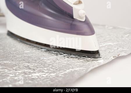 Le fer refait repasser la feuille sur un fond blanc. Nettoyage de la semelle du fer des dépôts de carbone par des méthodes populaires. Banque D'Images