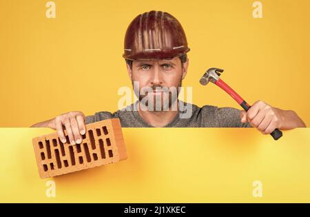 bricklayer. homme mature en casque avec marteau et brique. ouvrier barbu de constructeur Banque D'Images