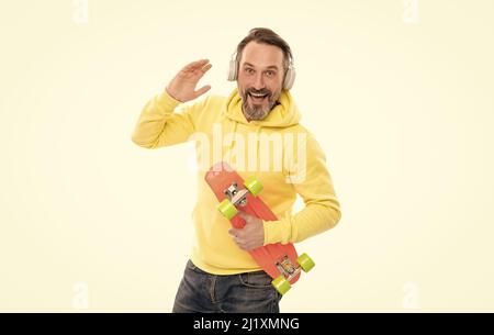 joyeux skateboarder écoutez de la musique dans les écouteurs tenez le skateboard isolé sur blanc, en s'amusant. Banque D'Images