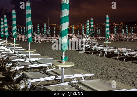 Parasols de plage, chaises longues et chaises sur une plage italienne au coucher du soleil tandis que la nuit tombe et les ombres s'allongent. Banque D'Images