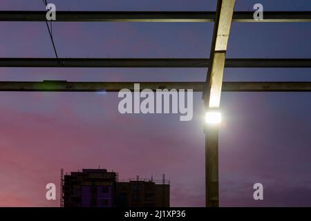 En regardant à travers une toile de poutres en acier, qui forit autrefois le toit d'un grand bâtiment avec le coucher de soleil coloré derrière et de petits projecteurs lumineux sur les montants verticaux. Banque D'Images