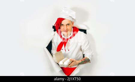 Un homme beau avec des dreadlocks rouges le tient dans ses œufs de poulet de main. Jeune cuisinier confiant en chemise blanche et cravate rouge tenant les oeufs de poulet, peeking th Banque D'Images