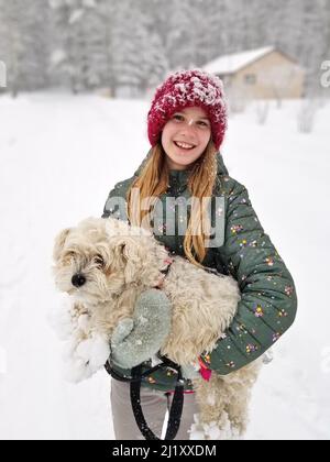 Portrait d'Une jeune fille souriante tenant son chien extrêmement Shaggy dont les griffes sont ancrées dans la neige Banque D'Images