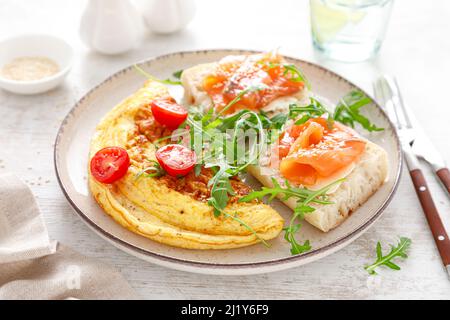 Omelette ou omelette, salade de tomates et d'arugula fraîches et toasts avec beurre et saumon salé. Petit déjeuner Banque D'Images