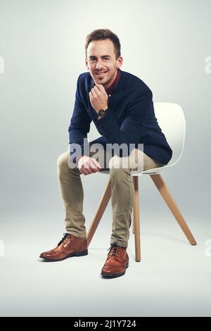 Je fais de mon entreprise le meilleur. Portrait studio d'un jeune homme d'affaires confiant assis sur une chaise sur un fond gris. Banque D'Images