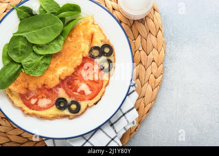 Omelette aux tomates, olives noires, fromage cottage et herbes aux épinards verts sur plaque blanche sur fond de béton gris. Délicieux petit déjeuner. En bonne santé Banque D'Images