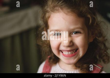 Portrait en gros plan d'une jolie petite fille blanche de race blanche avec un sourire tricheur et une expression sur son visage regardant directement l'appareil photo Banque D'Images