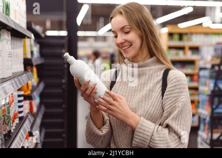 Jeune blond positif sélectionnant une bouteille de shampooing dans le magasin de cosmétiques Banque D'Images