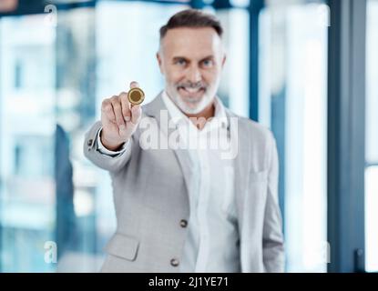 Bitcoin pourrait être votre billet d'ici. Photo d'un homme d'affaires mature tenant un bitcoin dans un bureau moderne. Banque D'Images