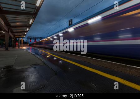 Le train Highland Caledonian Sleeper part de la gare de Preston avec un flou à l'aube montrant la ligne jaune sur la plate-forme de la gare Banque D'Images