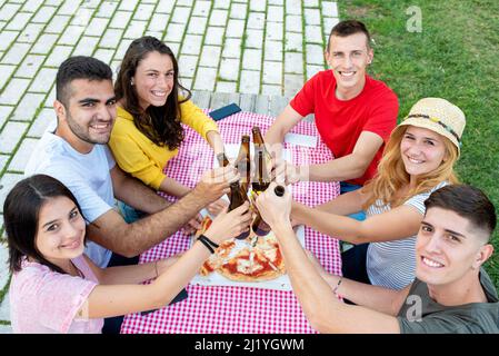 Couples engagés avec des bouteilles de bière, groupe d'amis ayant un pique-nique avec une pizza au parc, génération y personnes s'amusant et socialiser Banque D'Images