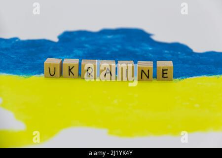 Le mot Ukraine écrit sur des cubes de bois sur fond avec la carte ukrainienne en bleu et jaune Banque D'Images