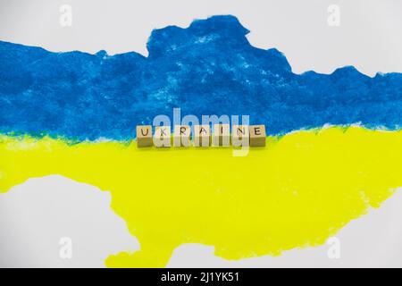 Le mot Ukraine écrit sur des cubes de bois sur fond avec la carte ukrainienne en bleu et jaune Banque D'Images