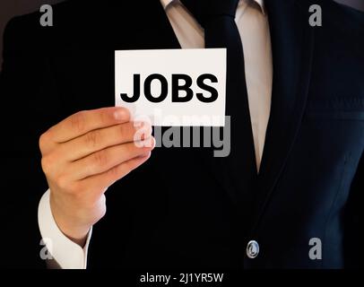 morceau de papier avec l'emploi d'inscription, concept de chômage dans le contexte de la crise mondiale, employé licencié, main sur un fond bleu Banque D'Images