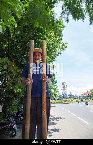 Un homme âgé qui se produit en marchant sur des pilotis sur le bord de la route près de Denpasar Bali, en Indonésie. Banque D'Images