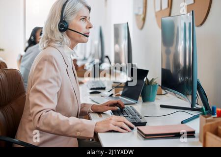 Donner l'exemple à mon équipe. Photo d'un agent mature assis au bureau et utilisant son ordinateur pendant que ses collègues travaillent derrière elle. Banque D'Images