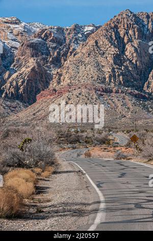 Las Vegas, Nevada, États-Unis - 23 février 2010 : zone protégée de Red Rock Canyon. La route asphaltée serpente sur un sol désertique sec avec des buissons menant à de grands b Banque D'Images