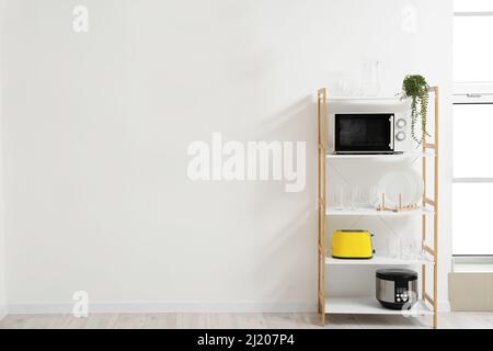 Étagère avec appareils de cuisson et vaisselle près du mur lumineux Banque D'Images