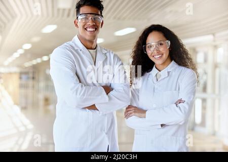 Scientifiques de l'avenir. Portrait court de deux jeunes étudiants en sciences debout avec leurs bras pliés dans un couloir du campus. Banque D'Images