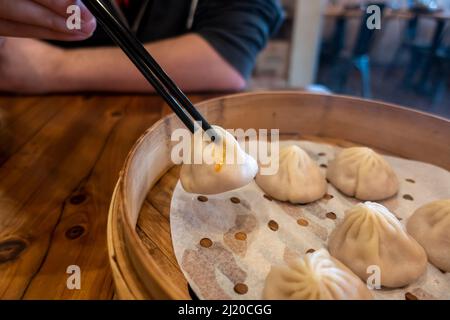 Vue rapprochée d'un homme prenant xiao long Bao dans un panier à vapeur à l'intérieur d'un restaurant Banque D'Images