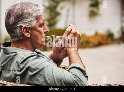 Il est temps de s'allumer. Coupe courte d'un homme âgé détendu qui fume un joint de marijuana tout seul à l'intérieur de son jardin à la maison pendant la journée. Banque D'Images