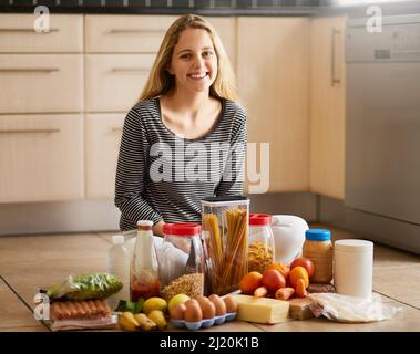 Passons à la cuisine. Photo d'une jeune femme attrayante entourée de divers aliments dans la cuisine à la maison. Banque D'Images