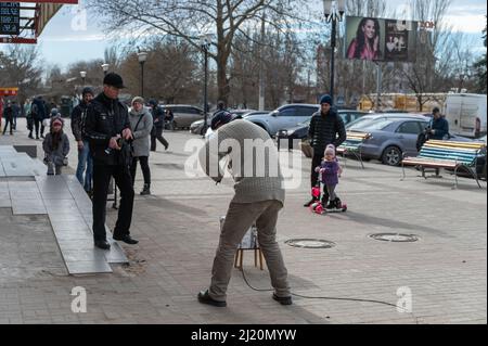 Le musicien de rue joue des instruments de musique devant le centre commercial. Homme mature avec un violon électronique. Les passants mettent de l'argent dans une boîte devant le Banque D'Images