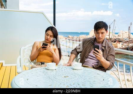 Jeune couple utilisant des téléphones cellulaires au café côtier près de la jetée de bateau de poisson - photo de stock Banque D'Images