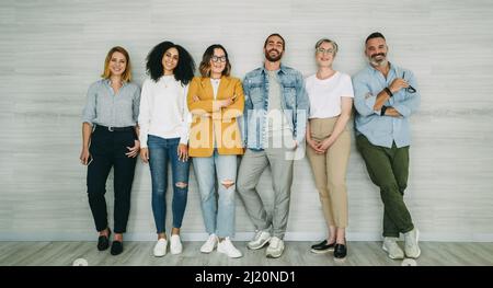 Divers hommes d'affaires souriant à la caméra tout en se tenant contre un mur. Groupe d'entrepreneurs réussis travaillant ensemble comme une équipe dans un Banque D'Images