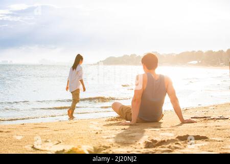 Un jeune homme assis sur la plage regardant une jeune femme - photo de stock Banque D'Images