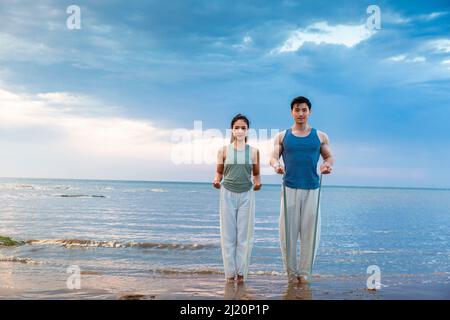 Jeune couple utilisant des bandes de résistance pour le yoga stretch à la plage - photo de stock Banque D'Images
