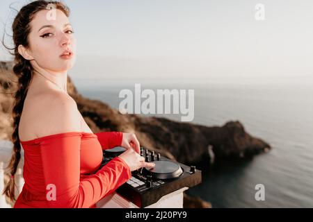 Les femmes du DJ jouent de la musique en mélangeant et en grattant le soir avec fond de mer et doux coucher de soleil chaud.Gros plan d'une console DJ contrôlée par Banque D'Images