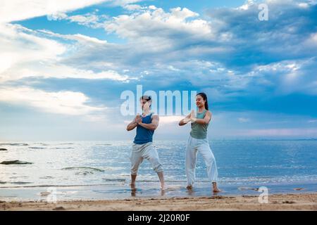 Jeune couple pratiquant la méditation de yoga en se tenant sur la plage - photo de stock Banque D'Images