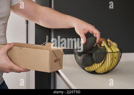 Gros plan des mains de l'homme en plaçant des avocats non mûrs sur un bol de fruits. Banque D'Images