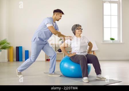 Un médecin de sexe masculin avec l'aide de fitball forme une patiente âgée dans une clinique de réadaptation. Banque D'Images