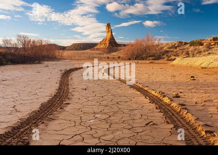 Traces de pneu dans la boue fissurée de rivière temporaire, Castildetierra formation de roche de montagne en arrière-plan, dans la lumière du soir. Parc naturel de Bardenas Reales. N Banque D'Images