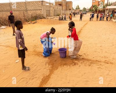 MBOUR, SÉNÉGAL, AFRIQUE - DÉCEMBRE CIRCA, 2021. De jeunes enfants africains non identifiés faisant une course de sacs dans la rue. Ils doivent remplir le bassin avec W Banque D'Images