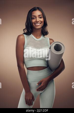 Le temps de travailler sur le corps de mes rêves. Photo d'une jeune femme attrayante debout seule dans le studio et tenant un tapis de yoga. Banque D'Images