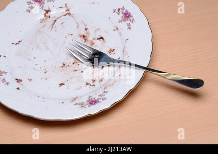 Assiette à gâteau sale avec fourchette argentée et dorée sur une table en bois Banque D'Images