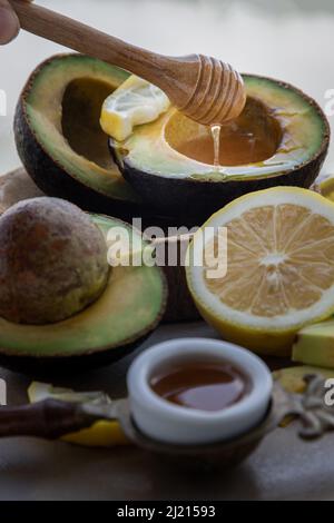 Gros plan de l'égouttement de miel de la pipette en bois sur l'avocat bio frais tranché en deux et le citron tranché avec le miel sur le plateau en céramique sain Banque D'Images