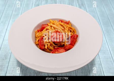 Pâtes italiennes de Bavette avec sauce tomate, parmesan et tomates cerises fraîches dans une assiette blanche sur une table en bois bleu clair Banque D'Images