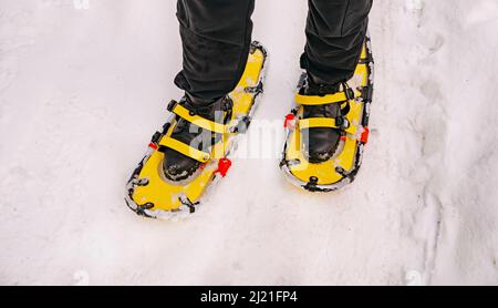 Raquettes jaunes sur bottes noires. Raquettes dans la forêt d'hiver dans la neige. Fermeture des jambes et des raquettes. Banque D'Images